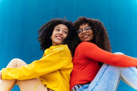 Téléchargez les photos : Jeunes femmes heureuses posant sur des murs colorés bleus et jaunes. Les adolescentes passent du temps ensemble après l'école - en image libre de droit