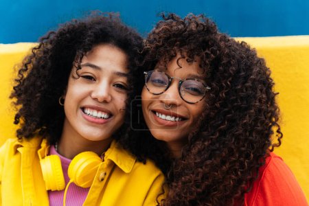 Foto de Mujeres jóvenes felices bailando y divirtiéndose al aire libre. Adolescentes escuchando música con smartphone y auriculares en una zona urbana moderna de color amarillo y azul - Imagen libre de derechos