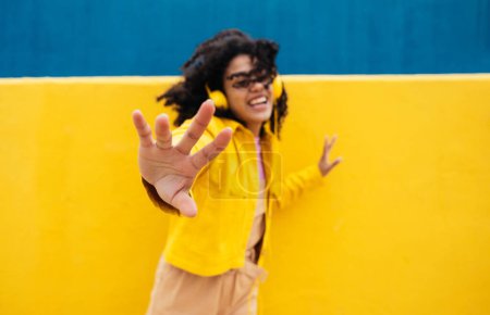 Photo for Young happy woman dancing and having fun outdoor. Teenager listening to music with smartphone and headphones in a yellow and blue modern urban area - Royalty Free Image