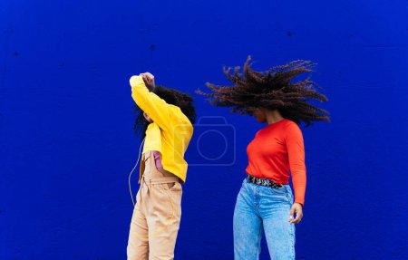 Photo for Young happy women dancing and having fun outdoor. Teenagers listening to music with smartphone and headphones in a yellow and blue modern urban area - Royalty Free Image