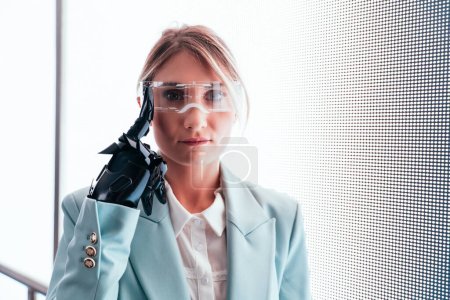 Photo for Business woman with cyborg bionic arm and augmented reality visor. Representation of the future that will include human being and tech parts - cyberpunk look - Royalty Free Image
