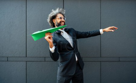 Cinematic and storytelling image of a young entrepreneur throwing a green paper aircraft in the air. Conceptual representation of green energy and technology ideas
