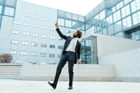 Téléchargez les photos : Jeune entrepreneur homme d'affaires écoutant de la musique et dansant à l'extérieur du bureau. Concept de liberté et de réussite en entreprise - en image libre de droit
