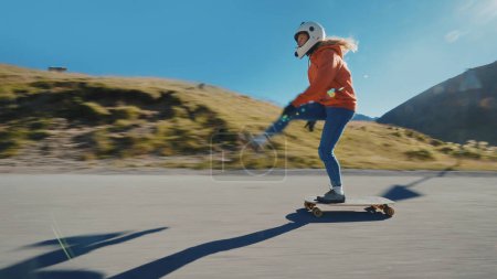 Foto de Sesión cinematográfica de longboard cuesta abajo. Mujer joven patinando y haciendo trucos entre las curvas en un paso de montaña. Concepto sobre deportes extremos y personas - Imagen libre de derechos