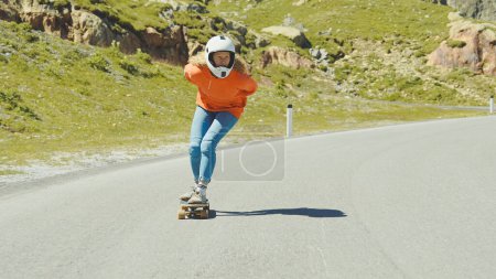 Téléchargez les photos : Séance de longboard en descente cinématographique. Jeune femme skateboard et faire des tours entre les courbes sur un col de montagne. Concept sur les sports extrêmes et les personnes - en image libre de droit