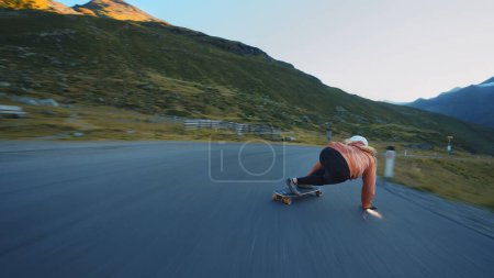 Foto de Sesión cinematográfica de longboard cuesta abajo. Mujer joven patinando y haciendo trucos entre las curvas en un paso de montaña. Concepto sobre deportes extremos y personas - Imagen libre de derechos