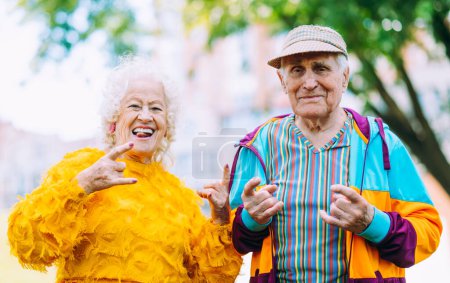 Téléchargez les photos : Vieux couple moderne habillage vêtements colorés à la mode. Jeune grand-mère et grand-père s'amuser en plein air et devenir sauvage. Représentation des personnes âgées se sentant jeunes à l'intérieur - en image libre de droit