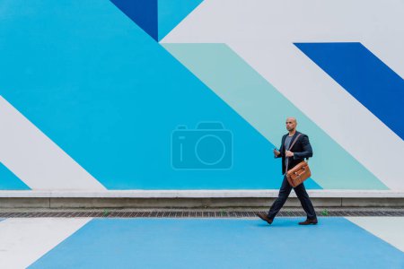 Photo for Young business man going to work in the morning passing by an urban area of the city with colored walls.Representation of a successful sales person reaching the top of the career. - Royalty Free Image