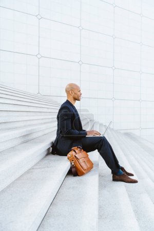 Photo for Young business man sitting and working in the financial street area of the city .Representation of a successful sales person reaching the top of the career. - Royalty Free Image