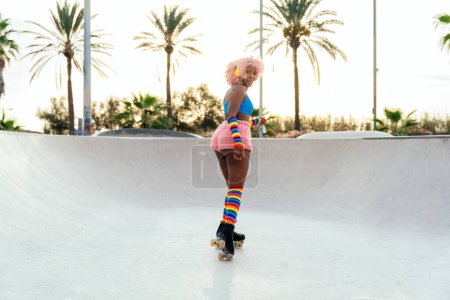 Schöne Frau, die mit Rollschuhen Schlittschuh läuft und Spaß hat. Professionelle Skater und Tänzer beim morgendlichen Training in farbenfroher und modischer Kleidung.