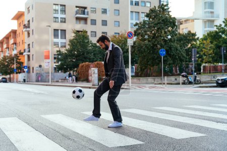 Téléchargez les photos : Image d'un homme d'affaires et joueur de soccer freestyle faisant des tours avec le ballon dans la rue. Concept sur le sport et les hommes d'affaires - en image libre de droit