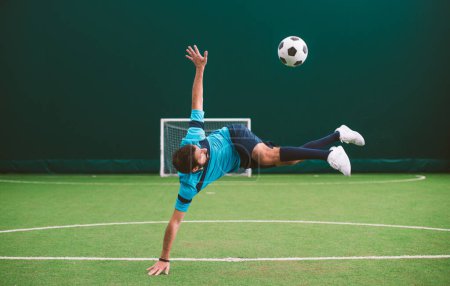 Foto de Imagen cinematográfica de un jugador de fútbol estilo libre haciendo trucos con la pelota en una cancha de césped artificial interior. Concepto sobre deporte y estilo de vida de las personas - Imagen libre de derechos