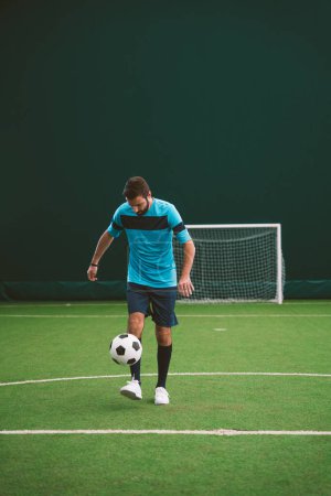 Foto de Imagen cinematográfica de un jugador de fútbol estilo libre haciendo trucos con la pelota en una cancha de césped artificial interior. Concepto sobre deporte y estilo de vida de las personas - Imagen libre de derechos