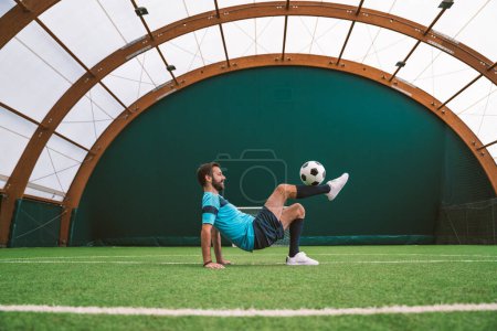 Téléchargez les photos : Image cinématographique d'un joueur de soccer freestyle faire des tours avec le ballon sur un terrain de gazon artificiel à l'intérieur. Concept sur le sport et le mode de vie - en image libre de droit