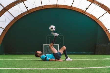 Téléchargez les photos : Image cinématographique d'un joueur de soccer freestyle faire des tours avec le ballon sur un terrain de gazon artificiel à l'intérieur. Concept sur le sport et le mode de vie - en image libre de droit