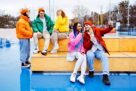 Foto de Grupo multirracial de jóvenes amigos felices que se reúnen al aire libre en invierno, vistiendo chaquetas de invierno y divirtiéndose, pareja tomando selfie en el teléfono inteligente para las redes sociales - Millennials multiétnicos que se unen en un área urbana, conceptos sobre la juventud y la liberación social - Imagen libre de derechos
