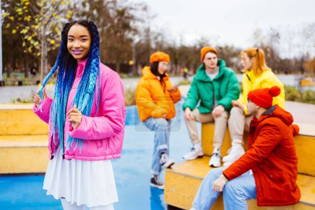 Foto de Grupo multirracial de jóvenes amigos felices que se reúnen al aire libre en invierno, vistiendo chaquetas de invierno y divirtiéndose, mujer negra de moda en primer plano - Millennials multiétnicos que se unen en un área urbana, conceptos sobre la juventud y las liberaciones sociales - Imagen libre de derechos
