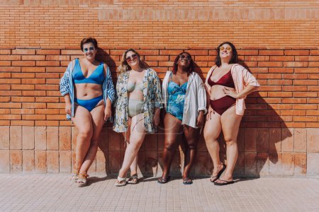 Photo for Group of beautiful plus size women with swimwear bonding and having fun at the beach, posing on a brick wall background - Curvy female friends enjoying summertime at the sea, concepts about body acceptance, body positive and self confidence - Royalty Free Image