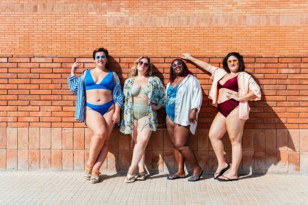 Foto de Group of beautiful plus size women with swimwear bonding and having fun at the beach, posing on a brick wall background - Curvy female friends enjoying summertime at the sea, concepts about body acceptance, body positive and self confidence - Imagen libre de derechos