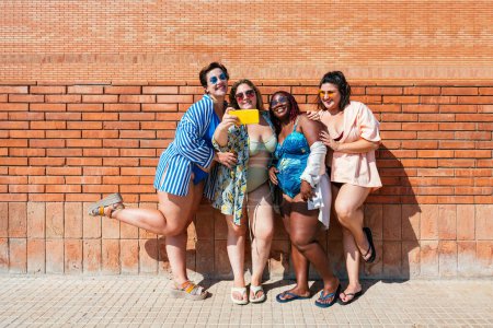 Téléchargez les photos : Group of beautiful plus size women with swimwear bonding and having fun at the beach, posing on a brick wall background - Curvy female friends enjoying summertime at the sea, concepts about body acceptance, body positive and self confidence - en image libre de droit