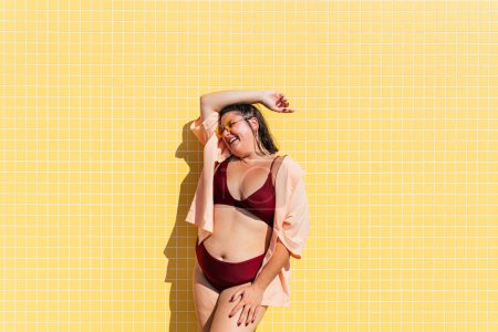 Téléchargez les photos : Beautiful and confident plus size woman having fun at the beach, posing on colorful wall background -  concepts about body acceptance, body positive, self confidence and body care - en image libre de droit