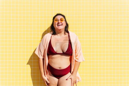 Téléchargez les photos : Beautiful and confident plus size woman having fun at the beach, posing on colorful wall background -  concepts about body acceptance, body positive, self confidence and body care - en image libre de droit