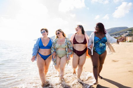 Foto de Group of beautiful plus size women with swimwear bonding and having fun at the beach - Group of curvy female friends enjoying summertime at the sea, concepts about body acceptance, body positive and self confidence - Imagen libre de derechos