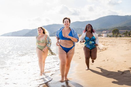 Téléchargez les photos : Group of beautiful plus size women with swimwear bonding and having fun at the beach - Group of curvy female friends enjoying summertime at the sea, concepts about body acceptance, body positive and self confidence - en image libre de droit