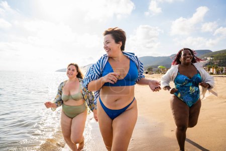 Téléchargez les photos : Group of beautiful plus size women with swimwear bonding and having fun at the beach - Group of curvy female friends enjoying summertime at the sea, concepts about body acceptance, body positive and self confidence - en image libre de droit