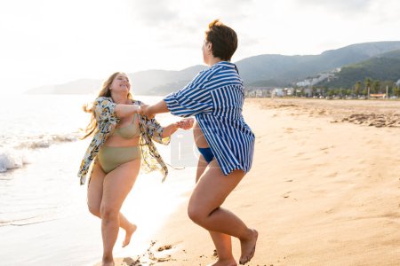 Foto de Two beautiful plus size women with swimwear bonding and having fun at the beach - Curvy female friends enjoying summertime at the sea, concepts about body acceptance, body positive and self confidence - Imagen libre de derechos