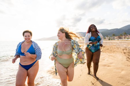 Foto de Group of beautiful plus size women with swimwear bonding and having fun at the beach - Group of curvy female friends enjoying summertime at the sea, concepts about body acceptance, body positive and self confidence - Imagen libre de derechos