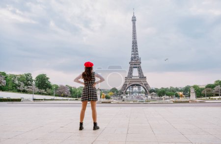 Téléchargez les photos : Beautiful young woman visiting paris and the eiffel tower. Parisian girl with red hat and fashionable clothes having fun in the city center and landmarks area - en image libre de droit