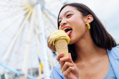 Photo for Beautiful young asian woman eating ice cream at amusement park - Cheerful chinese female portrait during summertime vacation- Leisure, people and lifestyle concepts - Royalty Free Image