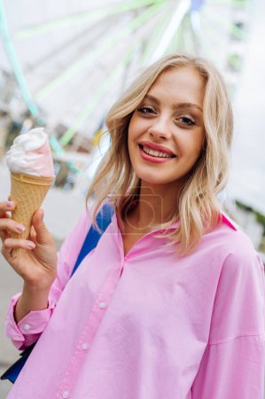 Foto de Beautiful young blond woman eating ice cream at amusement park - Cheerful caucasian female portrait during summertime vacation- Leisure, people and lifestyle concepts - Imagen libre de derechos