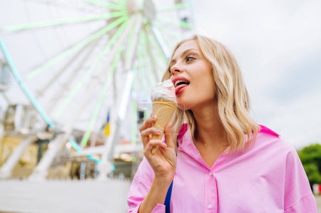 Foto de Beautiful young blond woman eating ice cream at amusement park - Cheerful caucasian female portrait during summertime vacation- Leisure, people and lifestyle concepts - Imagen libre de derechos