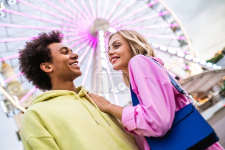 Photo for Multiracial young couple of lovers dating at theferry wheel in the amusement park - People with mixed races having fun outdoors in the city- Friendship, releationship and lifestyle concepts - Royalty Free Image