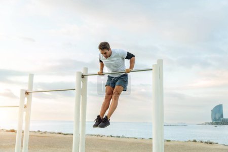 Foto de Sportive and athletic man doing functional training exercise at the outdoor gym - Adult athlete doing workout at sunrise at calisthenics park on the beach - Fitness, healthy lifestyle and sport concepts - Imagen libre de derechos