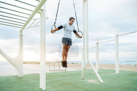 Téléchargez les photos : Sportive and athletic man doing functional training exercise at the outdoor gym - Adult athlete doing workout at sunrise at calisthenics park on the beach - Fitness, healthy lifestyle and sport concepts - en image libre de droit