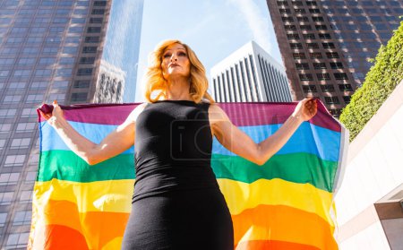 Foto de Transgénero mujer de negocios momentos de estilo de vida en el centro, Los Ángeles. Mujer transgénero sosteniendo una bandera arcoíris y defendiendo los derechos de la comunidad en una manifestación pública - Imagen libre de derechos