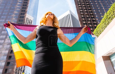 Photo for Transgender business woman lifestyle moments in downtown, Los angeles. Transgender woman holding a rainbow  flag and standing for the lgbt community rights at a public manifestation - Royalty Free Image