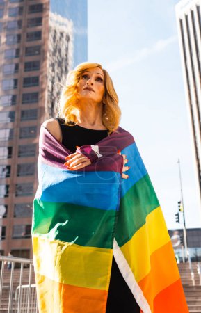Foto de Transgénero mujer de negocios momentos de estilo de vida en el centro, Los Ángeles. Mujer transgénero sosteniendo una bandera arcoíris y defendiendo los derechos de la comunidad en una manifestación pública - Imagen libre de derechos