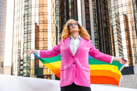 Téléchargez les photos : Transgenre business woman lifestyle moments in downtown, Los angeles. Femme transgenre tenant un drapeau arc-en-ciel et défendant les droits de la communauté d'lgbt lors d'une manifestation publique - en image libre de droit