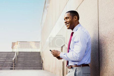 Téléchargez les photos : Handsome male african american business man CEO in a stylish corporate elegant suit in a business center outdoors - Black male commuter going to work, city and financial district in the background - en image libre de droit