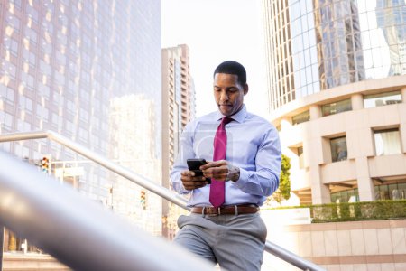 Photo for Handsome male african american business man CEO in a stylish corporate elegant suit in a business center outdoors - Black male commuter going to work, city and financial district in the background - Royalty Free Image