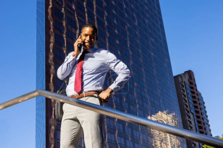 Photo for Handsome male african american business man CEO in a stylish corporate elegant suit in a business center outdoors - Black male commuter going to work, city and financial district in the background - Royalty Free Image