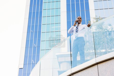 Foto de Hombre guapo afroamericano hombre de negocios CEO en un elegante traje corporativo elegante en un centro de negocios al aire libre - Negro viajero masculino que va a trabajar, ciudad y distrito financiero en el fondo - Imagen libre de derechos