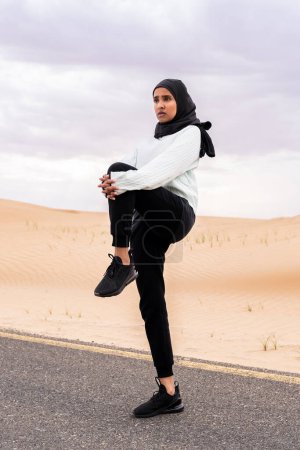 Photo for Beautiful middle-eastern arab woman wearing hijab training outdoors in a desert area - Sportive athletic muslim adult female wearing burkini sportswear doing fitness workout - Royalty Free Image