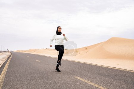 Photo for Beautiful middle-eastern arab woman wearing hijab training outdoors in a desert area - Sportive athletic muslim adult female wearing burkini sportswear doing fitness workout - Royalty Free Image