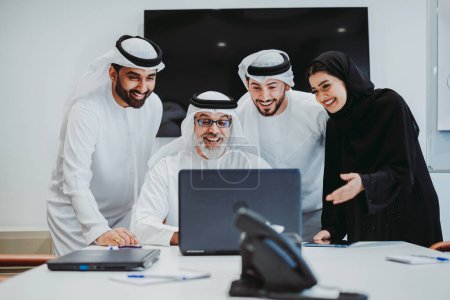 Photo for Group of middle-eastern corporate business people wearing traditional emirati clothes meeting in the office in Dubai - Business team working and brainstorming in the UAE - Royalty Free Image
