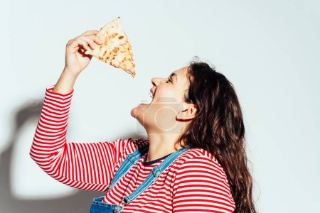 Foto de Modelo de mujer de talla grande posando en el estudio y divirtiéndose. Comer pizza italiana de la caja - Imagen libre de derechos